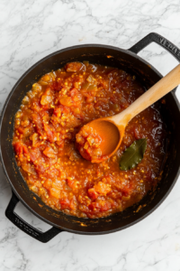 This image shows smooth, vibrant red tomato puree being added to the pan. The rich texture will create the perfect base for the Chicken Karahi’s bold and slightly tangy sauce.