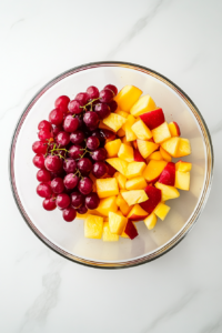 This image shows green and red grapes being sliced in half before being added to the fruit salad. This ensures a better texture and makes them easier to eat.