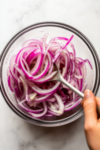 soaking-thinly-sliced-red-onions-in-water-to-mild-their-flavor
