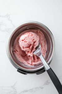 This image shows a top-down view of an ice cream maker churning the strawberry mixture into a thick and creamy texture, preparing it for freezing.