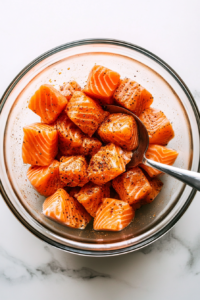 This image shows the salmon bites being generously coated with a fragrant spice mix, enhancing their flavor before cooking.