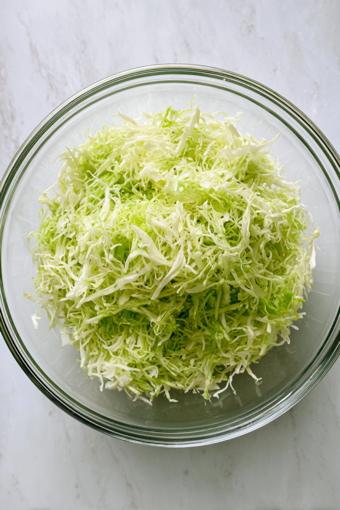 transferring-shredded-cabbage-to-large-glass-mixing-bowl-white-counter
