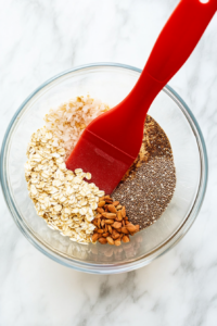 This image shows a top-down view of hearty rolled oats being poured into a bowl of thick peanut butter and honey mixture, blending the dry and wet ingredients to form the foundation of the lactation energy balls.