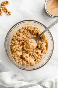 This image shows a top-down view of hands working through the oat and chocolate chip mixture, adjusting its consistency to achieve the perfect balance of stickiness and firmness for easy rolling into energy balls.