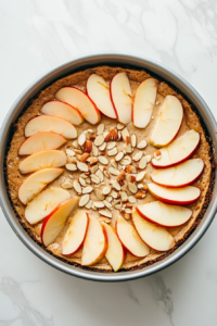 Neatly arranged apple slices on top of the cake batter, sprinkled with slivered almonds.