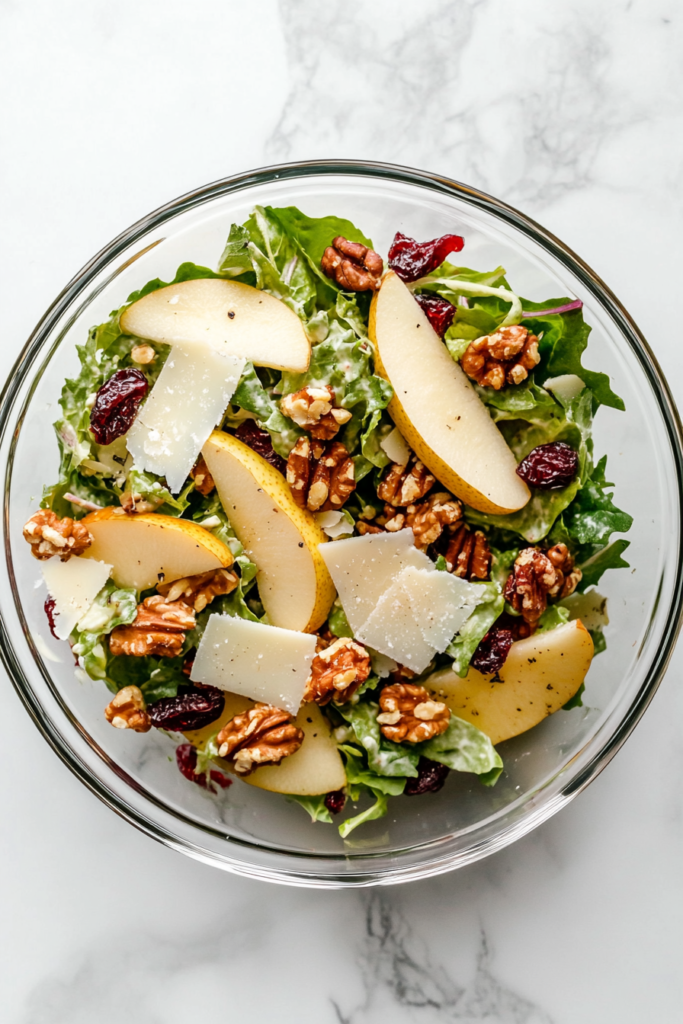 This image shows balsamic dressing being drizzled over a fully assembled autumn salad in a white bowl, with greens carefully layered to prevent wilting before serving.