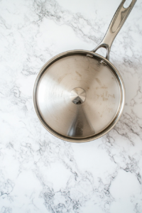 This image shows a covered saucepan with hard-boiled eggs sitting in hot water, undergoing the resting process for 10–12 minutes off the heat.
