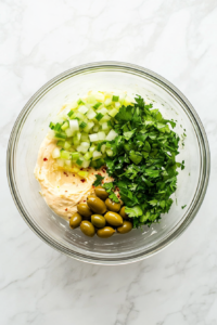 This image shows chopped herbs and finely diced vegetables being added to the remoulade base, bringing freshness and color to the sauce.