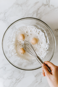 Eggs being whisked until light and frothy in a white ceramic bowl.