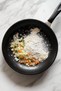 This image shows a black non-stick skillet on a white marble cooktop, with flour, granulated sugar, dried basil, salt, and pepper sprinkled over sautéed vegetables.