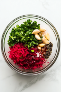 This image shows parsley, garlic, vinegar, oil, mustard, salt, and pepper being added to a bowl of grated beetroot, creating a vibrant and seasoned mix.