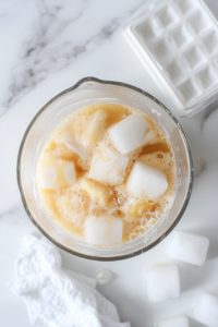 A close-up of ice cubes being added into a blender with the pina colada mixture, creating a frosty base for the drink.