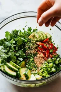 This image shows the finished Asian avocado salad topped with sesame seeds, chives, and cilantro, ready to serve in a round bowl.
