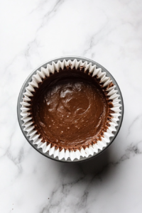 This image shows a 12-cup muffin pan with freshly baked chocolate cupcakes on a clean white marble countertop.