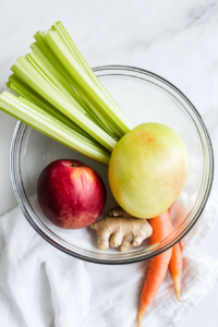 This image shows fresh produce including beetroot, apples, carrots, and celery being washed under cool running water in a kitchen sink, with droplets glistening and a clean, vibrant feel to the scene.
