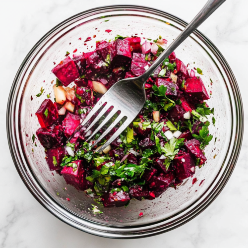 This image shows a vibrant beetroot salad served in a clear glass bowl, featuring grated beetroot topped with chopped parsley, minced garlic, vinegar, oil, mustard, salt, and pepper.