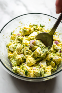 This image shows freshly ground black pepper and a pinch of salt being added to enhance the flavor of the avocado and egg mixture.