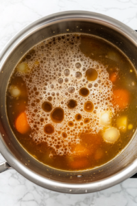 This image shows the pot of soup covered with a lid while simmering gently on a white marble countertop.