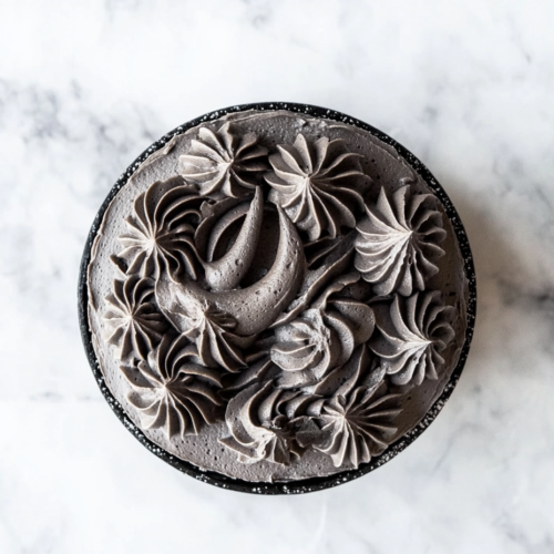 This image shows a top-down view of a celestial-themed Capricorn cake decorated with dark and light gray buttercream on a clean white marble countertop, styled with no background clutter.