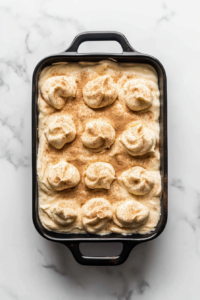 This image shows a baking dish with cinnamon filling dolloped over the batter, ready to be swirled, on white marble.