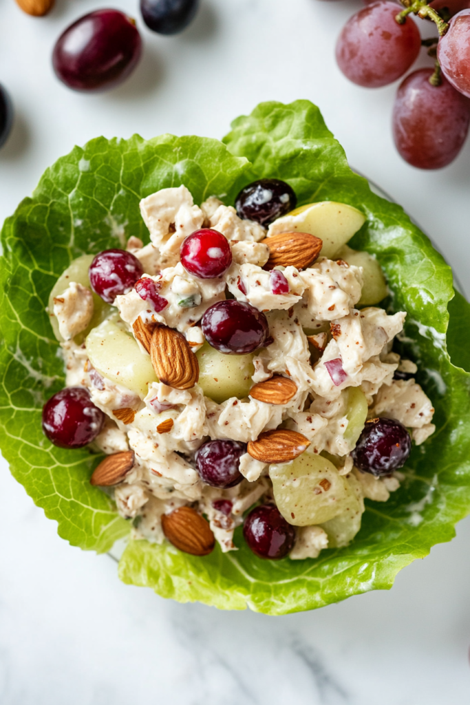 This image shows a close-up top-down view of a single lettuce wrap, highlighting the textures of the creamy chicken salad with visible grapes, almonds, and cranberries.