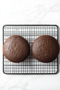 This image shows a top-down view of fully cooled chocolate cakes resting on a black wire rack placed over a white marble countertop, ready for slicing and serving.