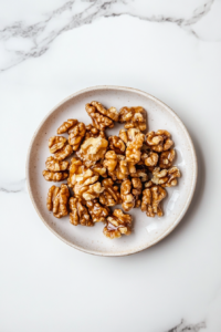 This image shows freshly candied walnuts spread out evenly on a parchment-lined plate to cool and crisp before being added to the salad.