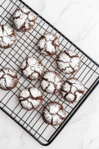This image shows chocolate crinkle cookies cooling on a black wire rack over a clean white marble countertop.