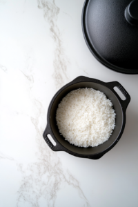 This image shows a black skillet covered with a matching black lid, resting undisturbed on a white marble countertop.