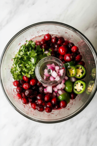 This image shows cranberries, green jalapeños, and chopped onions placed in a food processor, ready to be pulsed into a vibrant and tangy dip base.