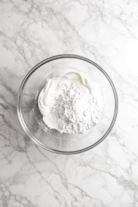 This image shows soft butter being creamed and blended with melted white chocolate in a mixing bowl, forming a smooth and luscious base.