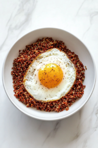 This image shows the steaming quinoa and freshly scrambled eggs being gently spooned into a bowl, forming the base of a hearty breakfast.