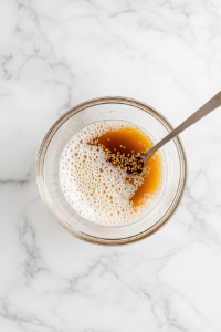 This image shows a small bowl filled with dressing ingredients being stirred together until silky and well combined.