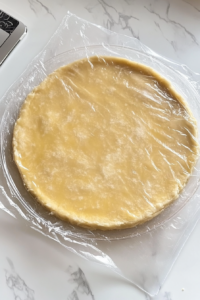 This image shows the finished dough pressed into a flat disc and neatly wrapped in plastic wrap, ready for chilling.