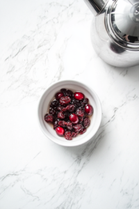 This image shows dried cranberries soaking in a bowl of hot boiling water, becoming plump and juicy to prepare them for blending into the dip.