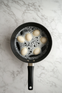 This image shows eggs submerged in rapidly boiling water, with bubbles rising around them, marking the beginning of the cooking process.
