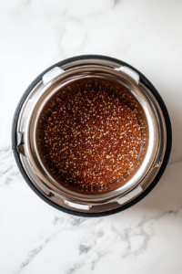 This image shows uncooked quinoa and water placed in a rice cooker, beginning to steam and soften into a fluffy, protein-packed grain.