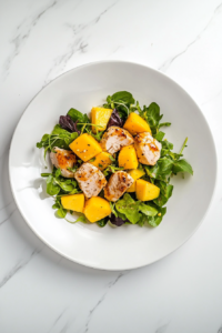 This image shows a finished chicken mango avocado salad plated on a white ceramic plate with spicy lime dressing drizzled over the top, resting on a white marble countertop.