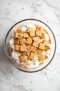 first-layer-of-crushed-graham-crackers-being-added-to-the-bottom-of-a-glass-trifle-bowl