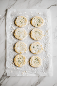 This image shows flattened biscuit dough rounds placed evenly on top of the creamy chicken mixture in a white baking dish, on a white marble cooktop.