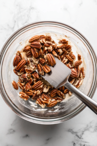 This image shows chopped pecans being gently folded into the sweet and sticky pie filling, adding a nutty crunch to every bite.