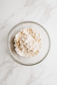 This image shows the chocolate Swiss roll batter evenly spread across the parchment-lined baking sheet on a white marble countertop.