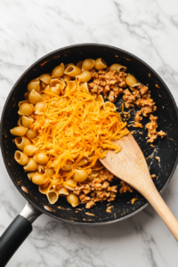 folding-shredded-cheddar-into-hot-cheeseburger-pasta-inside-black-skillet