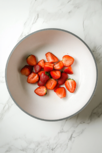 This image shows strawberries in a saucepan on medium-low heat, combined with sugar and lemon juice to create a rich sauce.