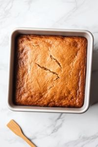 This image shows a freshly baked Parkin cake in the tin, showcasing its rich dark brown color and moist, dense texture straight from the oven.