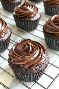 This image shows chocolate cupcakes topped with swirled chocolate frosting, placed neatly on a clean white marble countertop.
