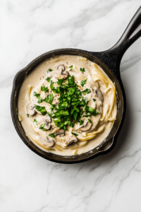 garnishing-mushroom-alfredo-with-chopped-cilantro-and-serving-in-a-white-bowl