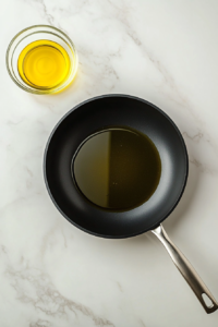 This image shows olive oil heating in a black skillet placed over a white marble cooktop, ready for cooking patties.