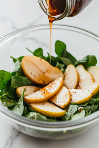 This image shows a large white bowl layered with crisp lettuce, delicate pear slices, shredded parmesan, tart dried cranberries, and crunchy candied walnuts, ready to be dressed.