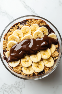 layers-of-sliced-bananas-and-drizzled-chocolate-ganache-being-added-over-graham-crackers